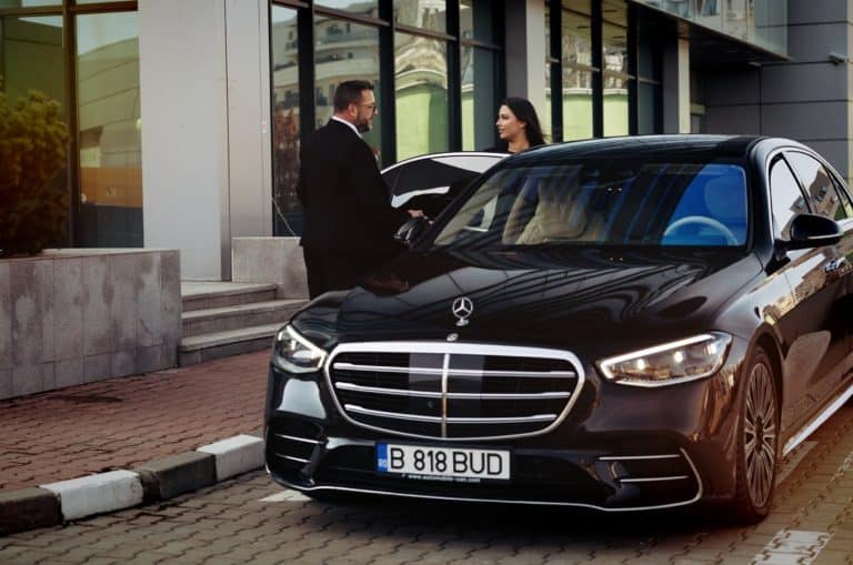 Professional chauffeur assisting a passenger at the rear door of a luxury sedan